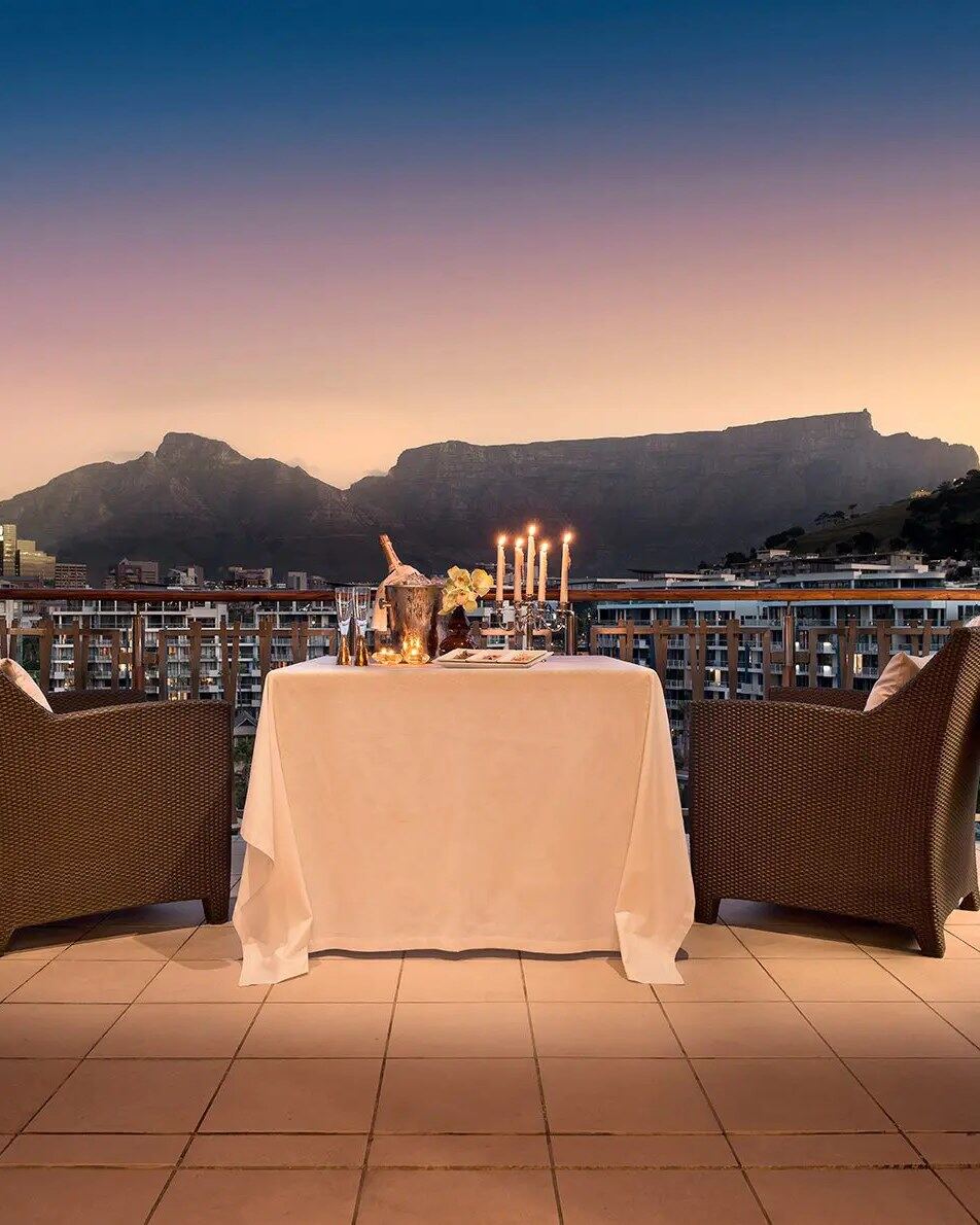 Styled private dinner table for two at dusk with candles and a mountain-and-sea view