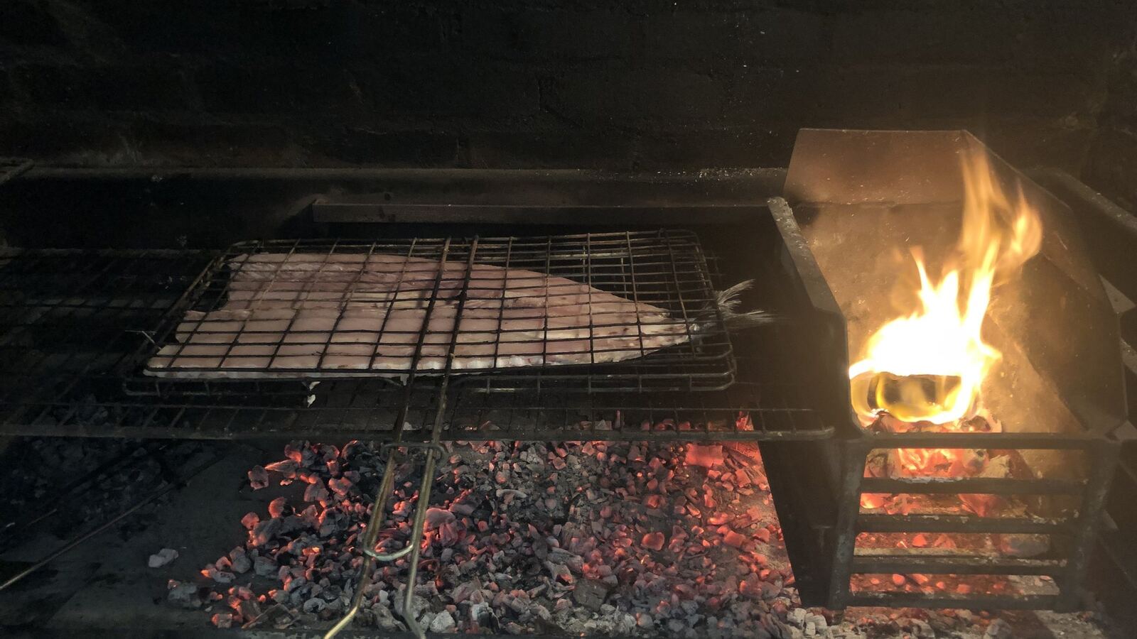Snoek grilling in a grid over glowing coals with flame